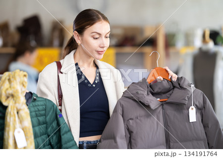 Attentive young woman choosing down jacket in clothing store 134191764