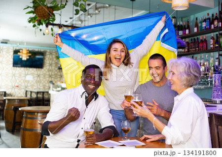 Excited male and female football fans celebrating championship win, waving flag of Ukraine in pub Excited male and female football fans celebrating championship win, waving flag of Ukraine in pub 134191800