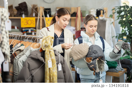 Discontented teen girl with mother choosing hat in clothing store Discontented teen girl with mother choosing hat in clothing store 134191818