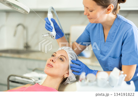 Adult woman cosmetologist doing moisturizing procedure to young woman Adult woman cosmetologist doing moisturizing procedure to young woman 134191822