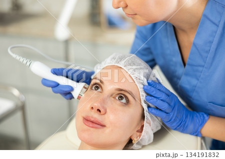 Adult woman cosmetologist doing ultrasound procedure to young woman Adult woman cosmetologist doing ultrasound procedure to young woman 134191832