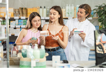 Woman with teen girl are busy choosing tablet pills at pharmacy. Man pharmacist in background Woman with teen girl are busy choosing tablet pills at pharmacy. Man pharmacist in background 134191928