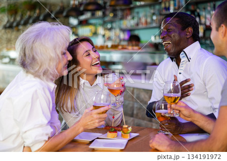 Diverse people talking and laughing drinking beer at a bar table Diverse people talking and laughing drinking beer at a bar table 134191972