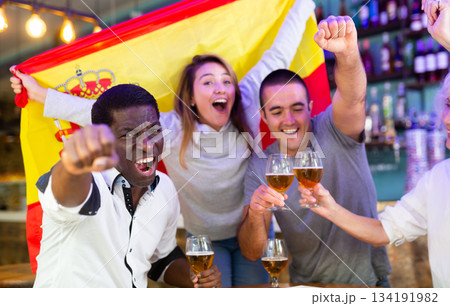 Spanish male and female soccer football fans celebrating championship win, waving flag of Spain in pub Spanish male and female soccer football fans celebrating championship win, waving flag of Spain in pub 134191982