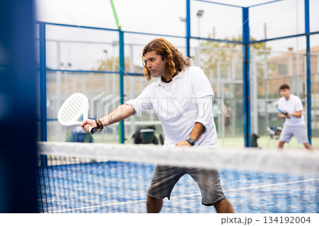 Sporty resolved man playing padel on open court 134192004