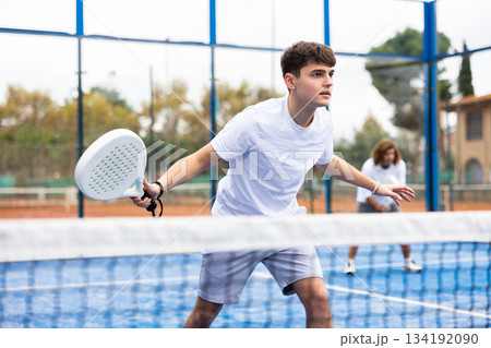 Young European male player serving ball during training padel in court outdoors in spring Young European male player serving ball during training padel in court outdoors in spring 134192090