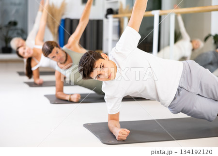 Positive athletic male performing set of exercises on a pilates mat during group class in fitness studio. Positive athletic male performing set of exercises on a pilates mat during group class in fitness studio. 134192120