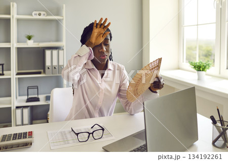 Exhausted woman at her workplace in office suffering from hot weather and lack of air conditioning. 134192261