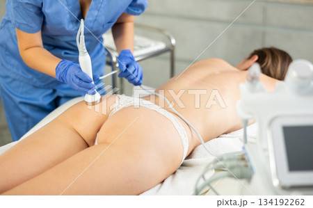 Adult woman cosmetologist gives ultrasonic massage of butt to young woman Adult woman cosmetologist gives ultrasonic massage of butt to young woman 134192262