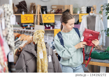 Happy teenage girl choosing ladies' handbag in clothing shop with large assortment Happy teenage girl choosing ladies' handbag in clothing shop with large assortment 134192272
