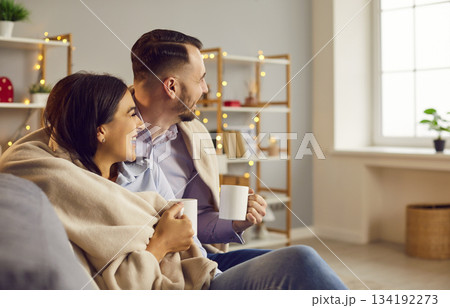 Couple sitting on sofa in the living room at home with a cup of tea or coffee and laughing. 134192273