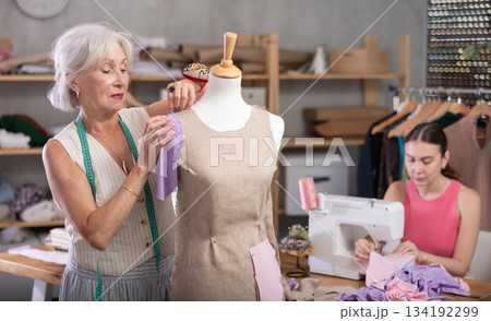 Adult woman sews on machine female assistant sews on mannequin 134192299