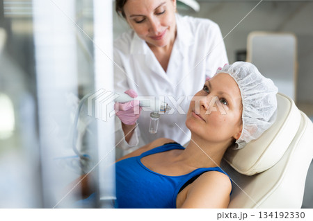 Young female cosmetologist doing moisturizing procedure to adult woman Young female cosmetologist doing moisturizing procedure to adult woman 134192330