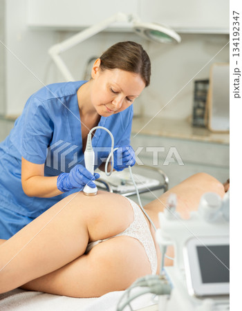 Adult woman cosmetologist gives ultrasonic massage of butt to young woman 134192347