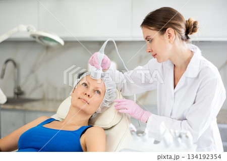 Young female cosmetologist doing whitening procedure to adult woman Young female cosmetologist doing whitening procedure to adult woman 134192354