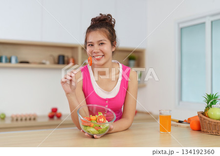 Joyful Eating. Woman smiling while enjoying fresh salad in kitchen. 134192360