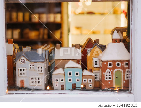 Miniature ceramic houses displayed in a shop window with warm festive lighting. 134192813