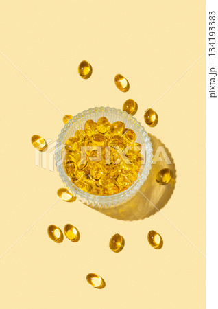 Yellow softgel vitamins capsules in a bowl on a bright background with shadow. 134193383