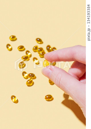 A hand holding a soft capsule containing D3 on a yellow background with shadow. 134193384