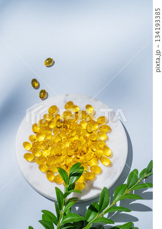 Yellow softgel vitamins capsules on a white marble plate with green leaves 134193385