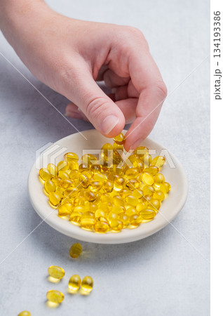 A hand holding a soft capsule containing D3 in a plate on a light background. 134193386