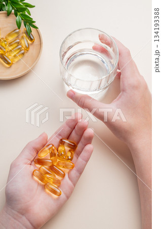 A hands holding yellow softgels and a glass of water on a yellow background. A hands holding yellow softgels and a glass of water on a yellow background. 134193388