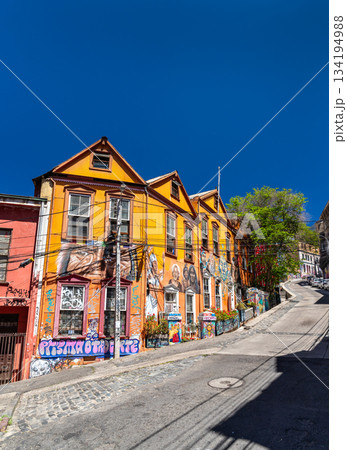 Valparaiso, Chile - October 17, 2025: Colorful houses with street art murals on Almirante Montt street. The steep cobblestone road winds through the historic Cerro Alegre district under a blue sky Valparaiso, Chile - October 17, 2025: Colorful houses with street art murals on Almirante Montt street. The steep cobblestone road winds through the historic Cerro Alegre district under a blue sky 134194988