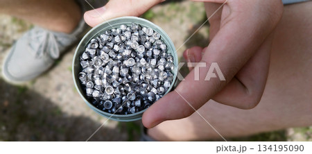 Close-up, high-angle shot of a container filled with silver airgun pellets, held carefully in two human hands outdoors. Shallow depth of field blurs the background Close-up, high-angle shot of a container filled with silver airgun pellets, held carefully in two human hands outdoors. Shallow depth of field blurs the background 134195090