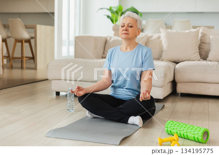 Yoga mindfulness meditation. Senior adult mature woman practicing yoga at home. Mid age old lady sitting in lotus pose on yoga mat meditating relaxing. Older middle aged woman doing breathing practice 134195775