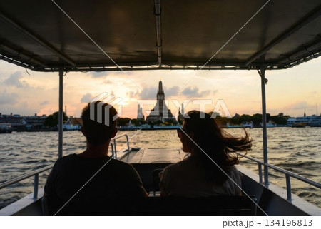 Over-the-shoulder view of foreign travelers on a Thai ferry looking toward Wat Arun at sunset 134196813