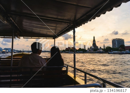 Over-the-shoulder view of foreign travelers on a Thai ferry looking toward Wat Arun at sunset 134196817
