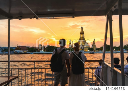 Over-the-shoulder view of foreign travelers on a Thai ferry looking toward Wat Arun at sunset 134196838