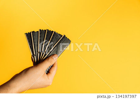Hand holding fan of black DDR RAM sticks on yellow background, upgrade concept Hand holding fan of black DDR RAM sticks on yellow background, upgrade concept 134197397