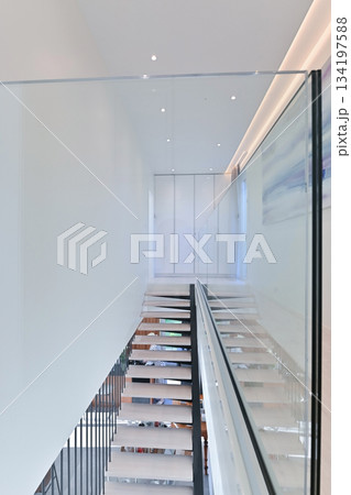 Bright minimalist hallway with floating staircase, glass railing, white walls, and abstract artwork in a modern luxury home interior with clean architectural lines Bright minimalist hallway with floating staircase, glass railing, white walls, and abstract artwork in a modern luxury home interior with clean architectural lines 134197588
