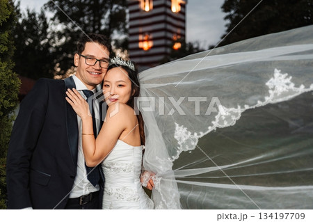 Interracial couple celebrating wedding day with flowing veil Interracial couple celebrating wedding day with flowing veil 134197709