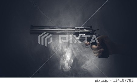 Hand holding a revolver in a dark, smoky atmosphere. The image evokes a sense of suspense and danger. Concept of Gun Violence 134197793