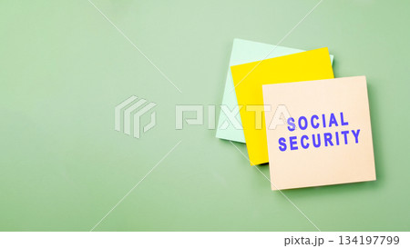 Top view of a stack of three square sticky notes in yellow, light green, and beige with the words SOCIAL SECURITY printed in blue, set against a pastel green background. Concept of social security 134197799