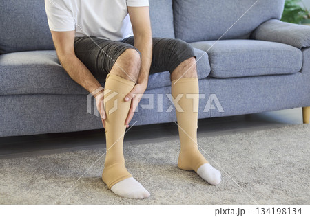 Man massaging calf while wearing compression socks for vein health at home Man massaging calf while wearing compression socks for vein health at home 134198134
