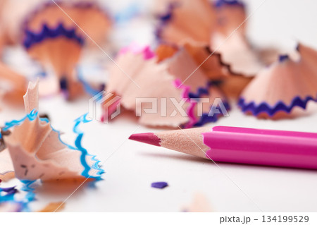 Bright pink pencil lying on a white surface surrounded by multi-colored pencil shavings Bright pink pencil lying on a white surface surrounded by multi-colored pencil shavings 134199529