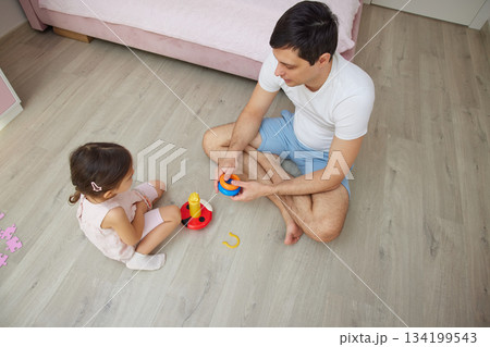 Father and daughter sitting on floor at home, bonding while playing with colorful toys 134199543