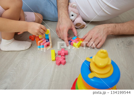 close-up of father and daughter sitting on floor at home, bonding while playing with colorful toys 134199544
