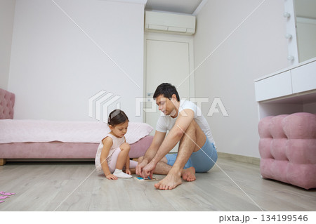Father and daughter enjoying time together, solving a puzzle on the bedroom floor Father and daughter enjoying time together, solving a puzzle on the bedroom floor 134199546