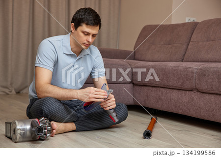 Man sitting on floor assembling parts of a vacuum cleaner 134199586