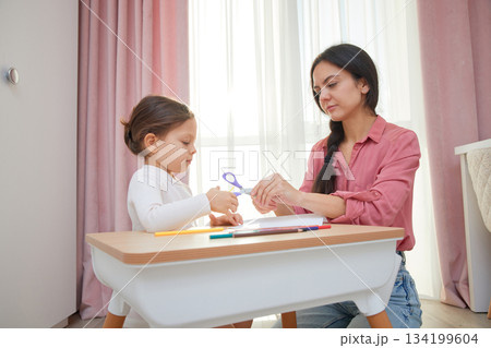 Mother and daughter cutting designs from paper with scissors for an art project 134199604