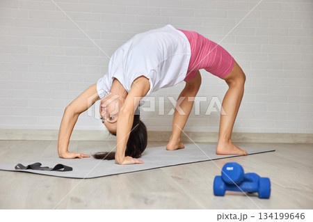 Woman performing a yoga bridge pose on a mat during home fitness routine Woman performing a yoga bridge pose on a mat during home fitness routine 134199646