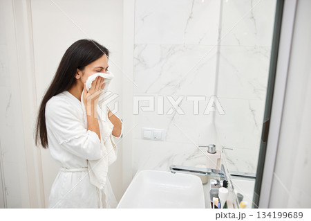Young woman drying her face with a soft white towel in a clean bathroom 134199689
