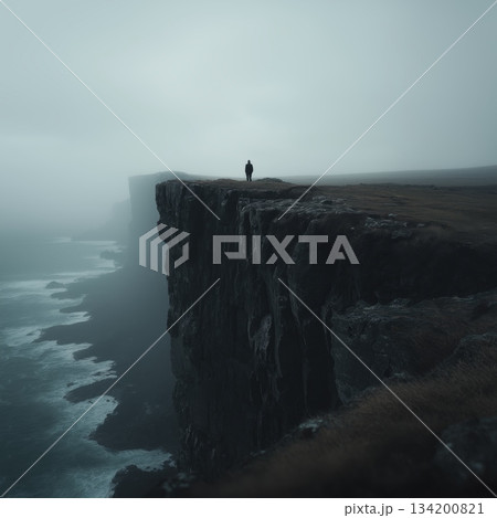 Lone figure standing on a cliff edge facing a dark, misty sea. Figure on a cliff overlooking waves in a gloomy, mysterious, and atmospheric landscape 134200821