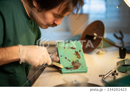 Master repairing retro lamp at workshop, scraping off old paint from base, creative working process. 134201423