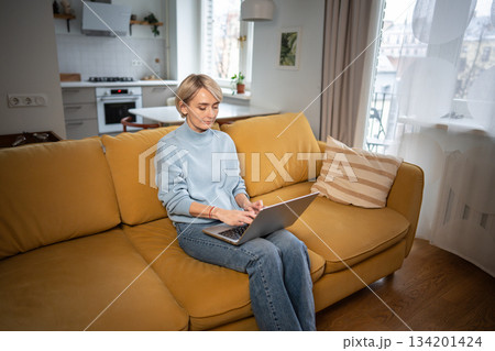 Relaxed middle aged business woman typing on laptop while sitting on comfy couch at home in room. 134201424
