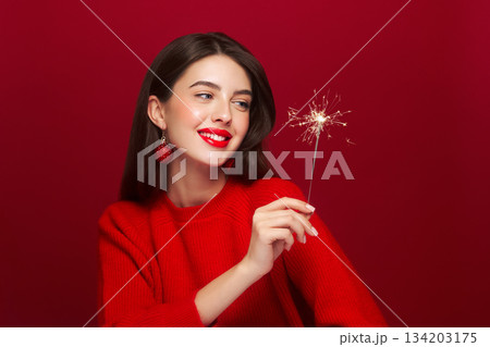 Beautiful young woman holds a sparkler on red background 134203175